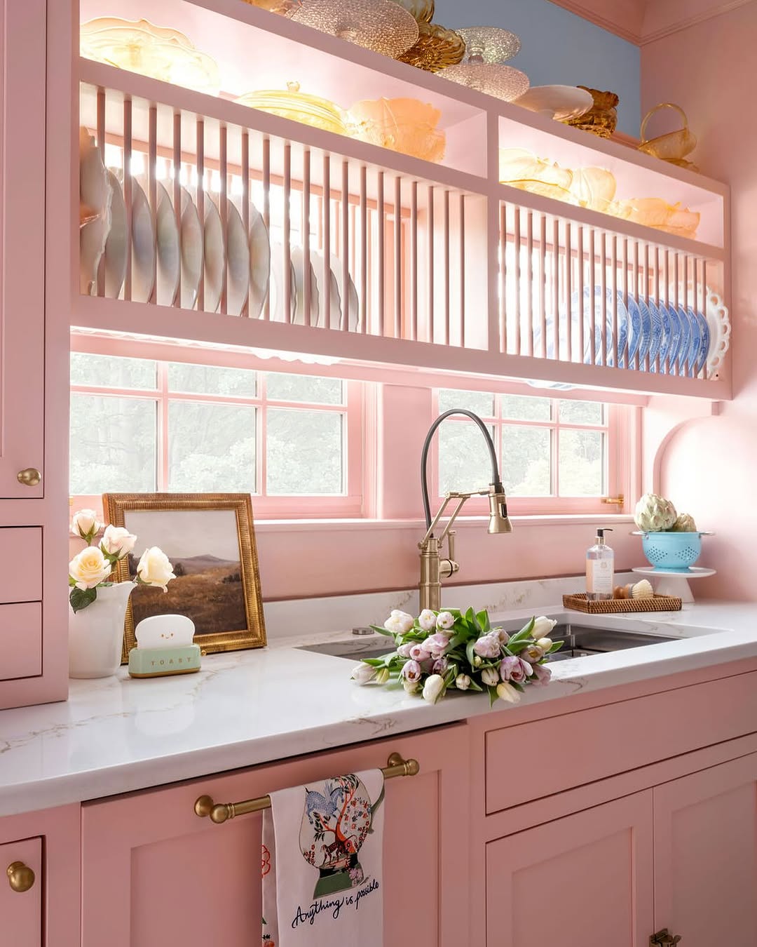 A modern pink kitchen with glossy hot pink cabinets, gold hardware, a black marble countertop, and an antiqued mirrored backsplash.