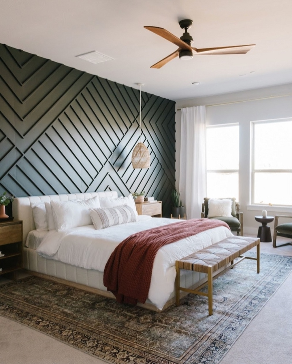 Modern bedroom with a geometric bedroom accent wall, white bedding, a rust-colored throw, wooden furniture, and large windows letting in natural light.