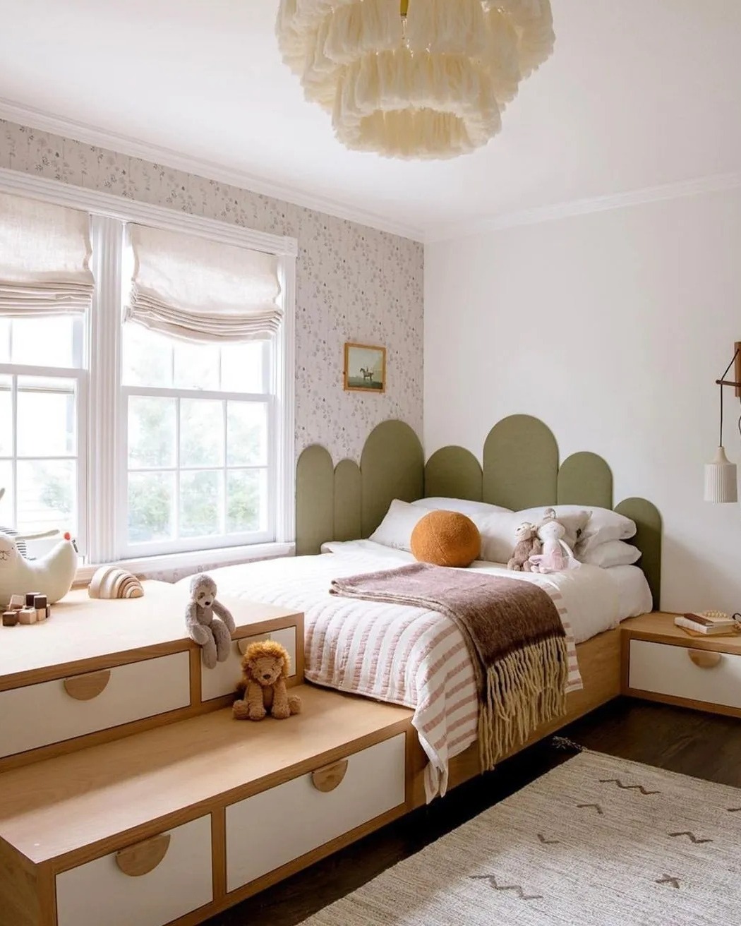 A cozy teen girl bedroom featuring a scalloped green headboard, built-in storage drawers, soft toys on the bed, and natural light from two large windows.
