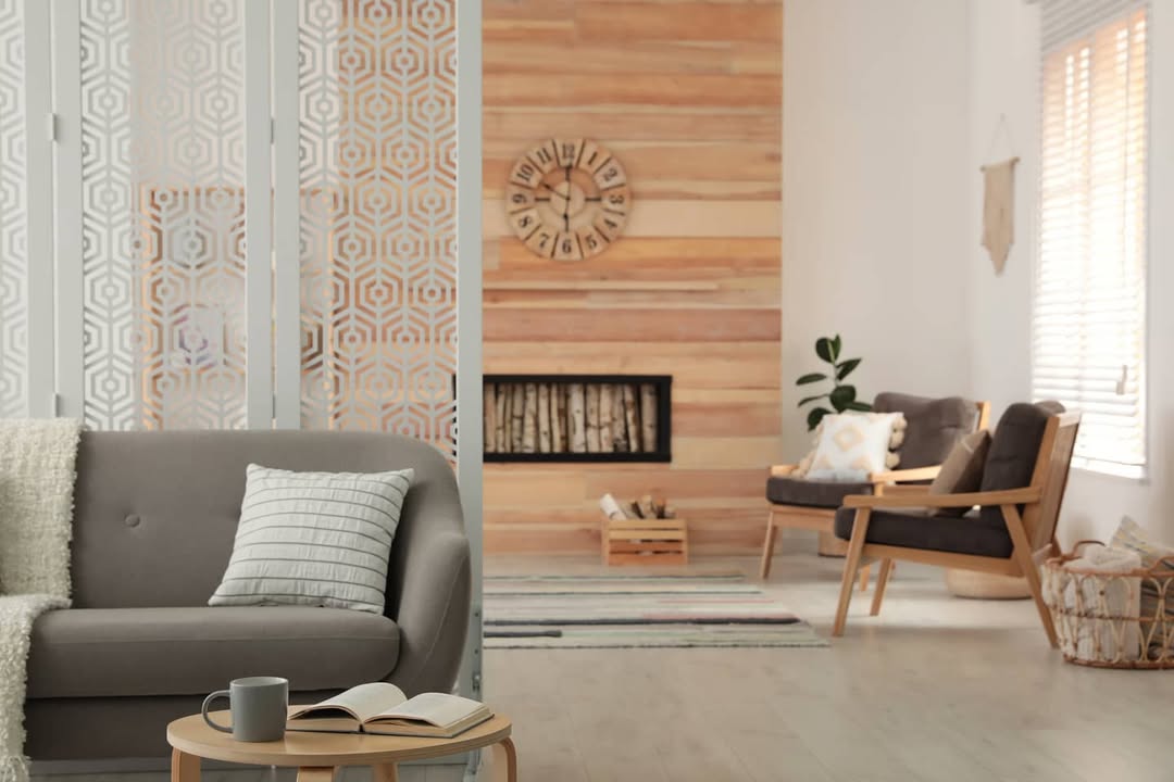 A modern living room with a grey sofa, wooden coffee table, armchairs, wall clock, and fireplace showcases neutral tones and geometric patterns—perfect for stylish homeowners seeking instant style.