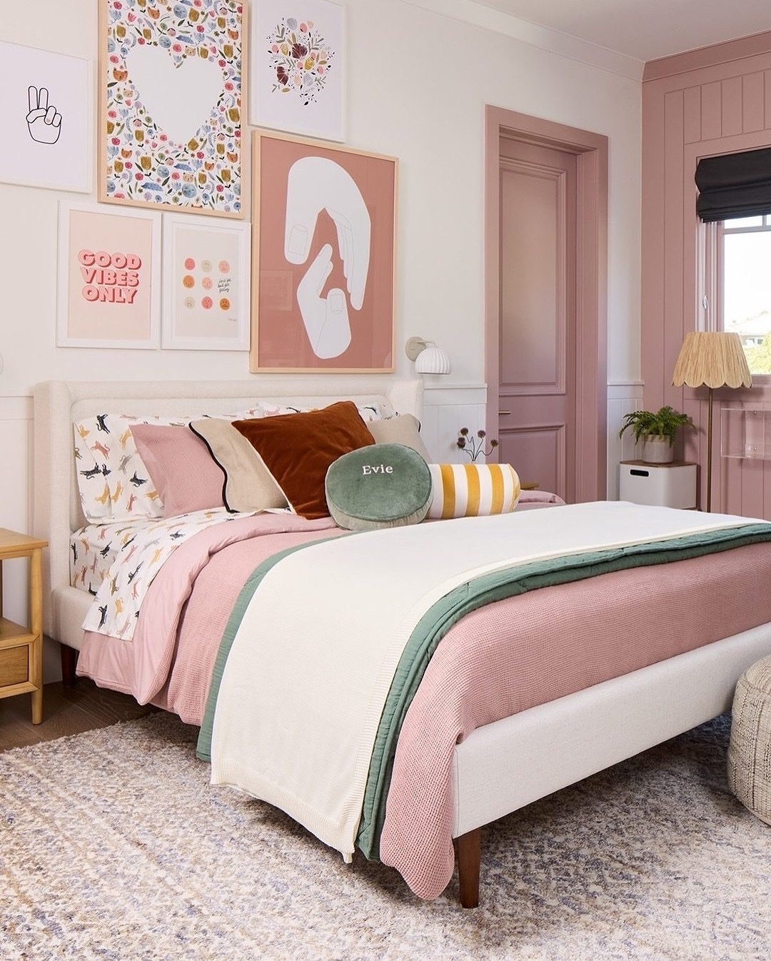 A neatly made bed with sage green and blush pink bedding, decorative pillows, and framed art on the wall in a cozy, pastel-themed bedroom.