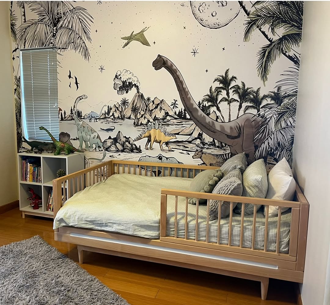 The children's room features a vibrant dinosaur-themed mural, perfect for inspiring adventure. A cozy daybed adorned with multiple pillows awaits explorers, while to the left, a small bookshelf completes this delightful dinosaur bedroom setup.