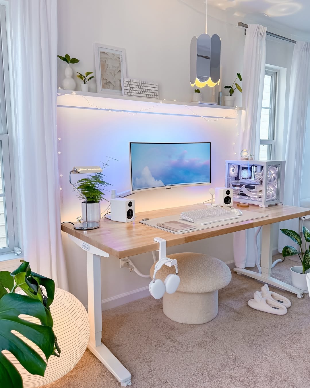 A minimalist office design featuring a computer desk setup with a monitor, white keyboard, speakers, potted plant, and LED lights, complemented by modern decor and bright natural lighting for inspiration.