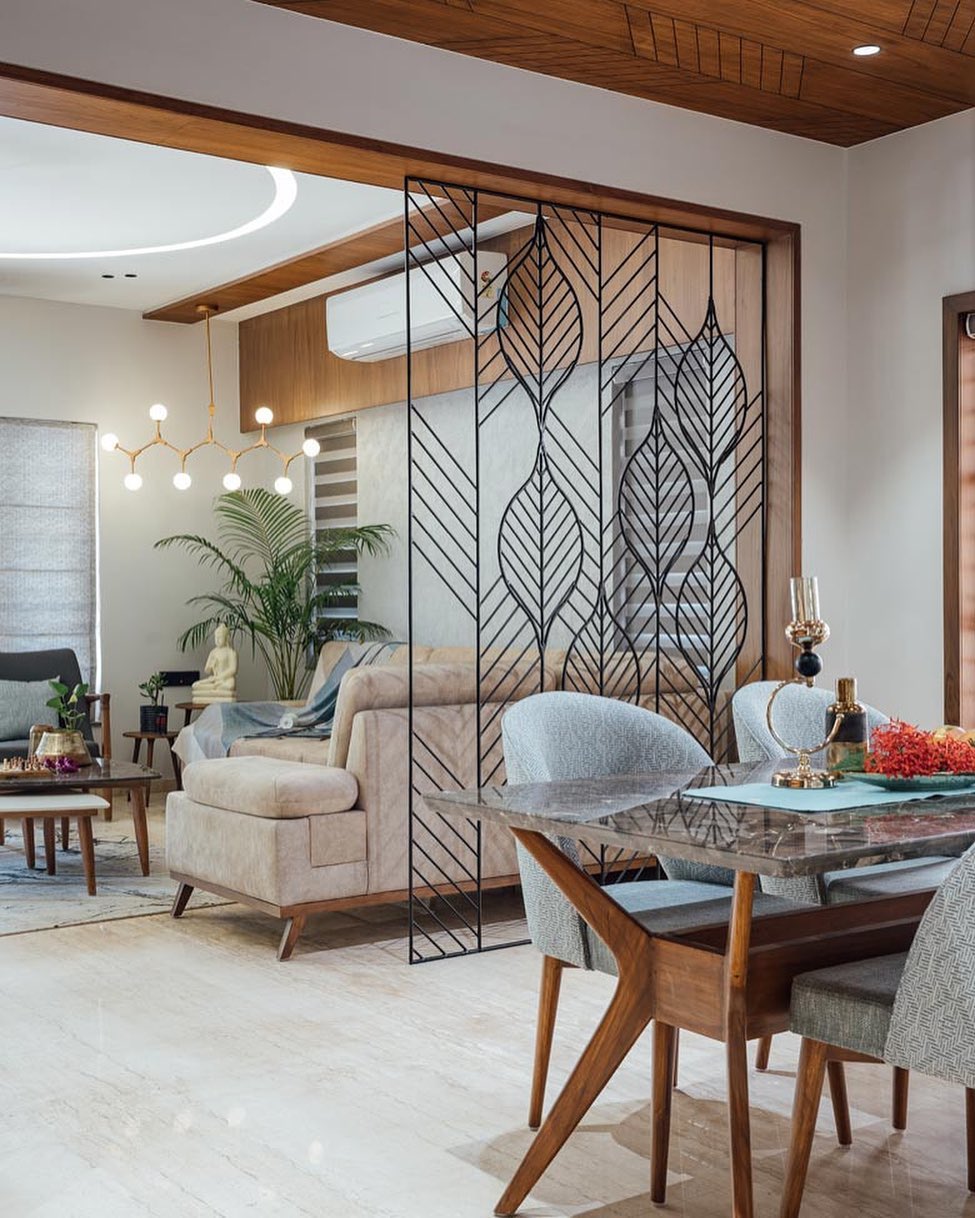 Modern living and dining area separated by a decorative black metal leaf-patterned partition—perfect for stylish homeowners seeking instant style with unique divider screen ideas, complemented by neutral furnishings and wood accents.