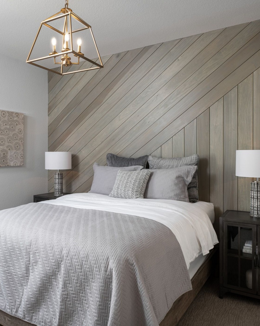 A modern bedroom with a green bedroom accent wall, beige upholstered bed, wooden bench, two nightstands with lamps, and a brass chandelier overhead.