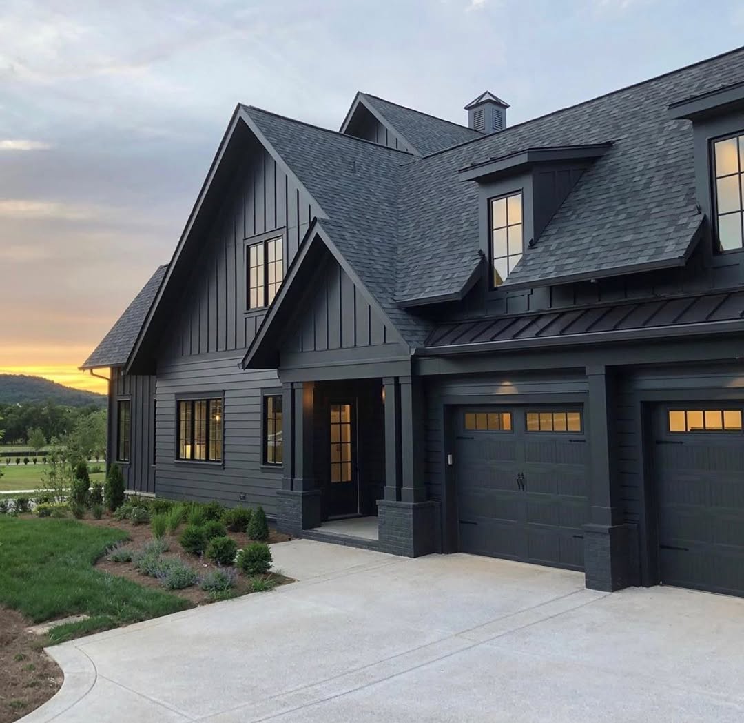 A modern two-story Black and Cedar House with dark exterior siding, large windows, and a double garage, set against a backdrop of greenery at sunset—perfect for those seeking inspiring house exterior ideas.