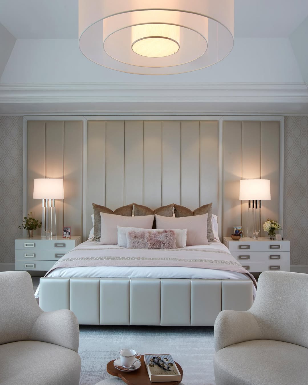 Modern bedroom with a dark upholstered bed as the bed focal point, gray bedding, two bedside tables with lamps, and illuminated built-in shelves displaying decor and books above the headboard.