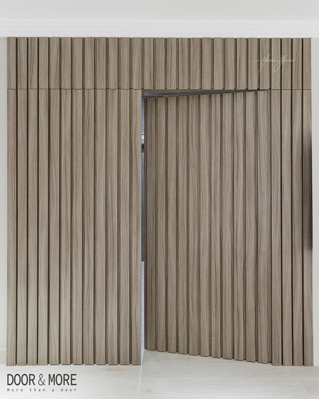 A modern folding wooden partition door with vertical panels, partially open, set against a light-colored wall and floor. Perfect for stylish homeowners seeking hidden door ideas.