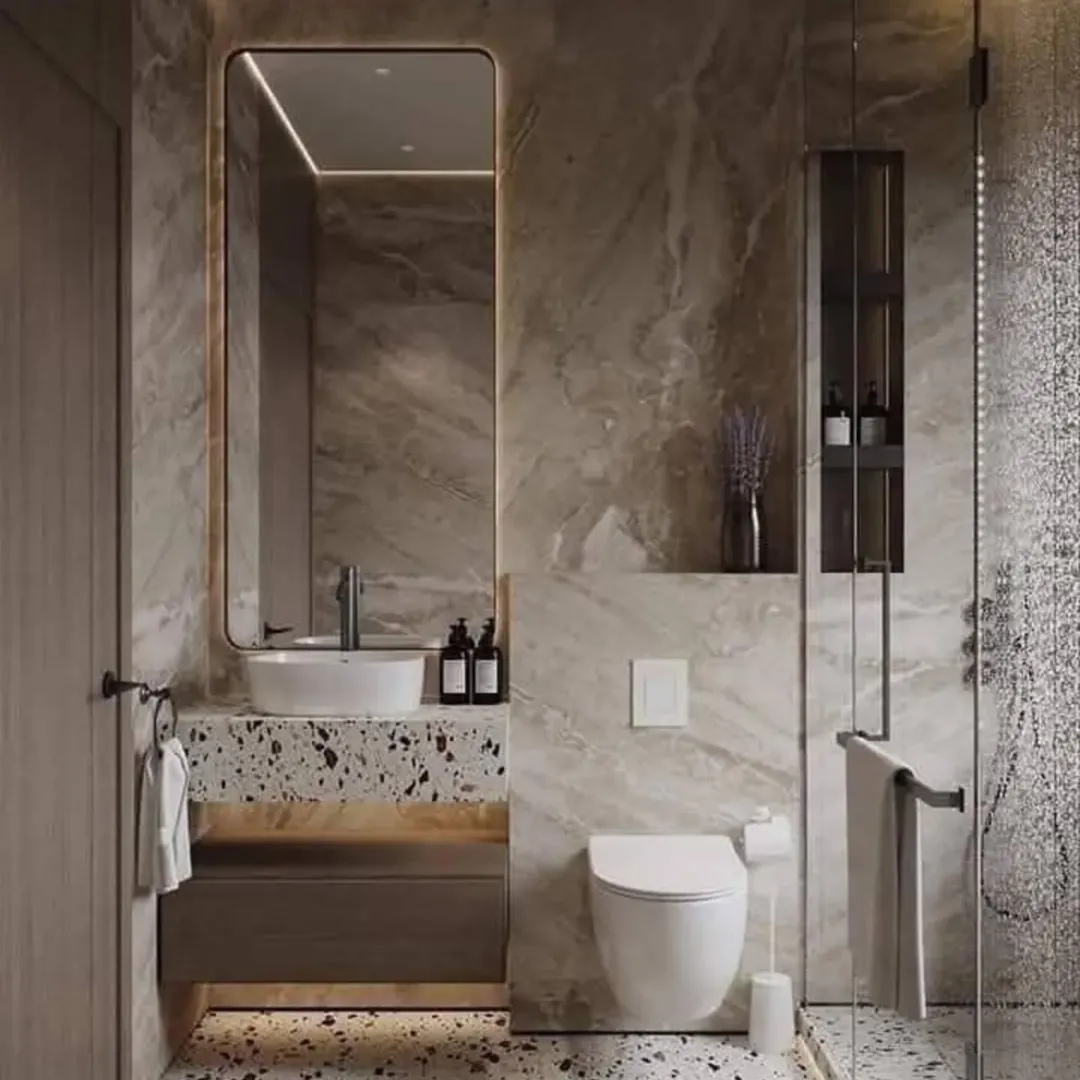 A small bathroom with a round mirror, white sink, toilet, shelf with plants and toiletries, gold accents, and a window with natural light. Leaf-patterned wallpaper covers one wall—perfect for inspiring your next Half Bathroom Decor update.