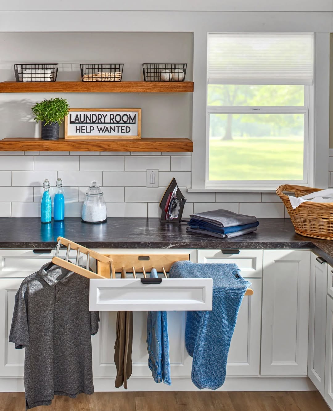 Modern laundry room with front-loading washer and dryer, featuring stylish laundry room shelves that hold baskets, jars, and plants, plus a small black step stool placed in front of the appliances.