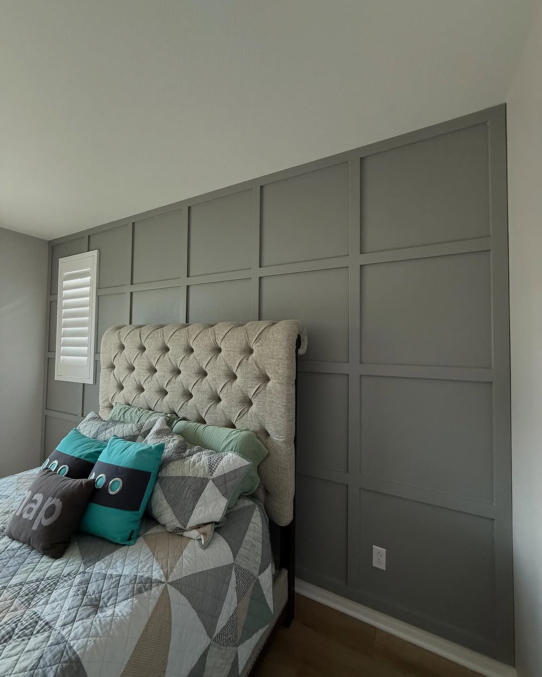 A bed with pillows and a headboard sits in a room featuring a stylish bedroom accent wall.