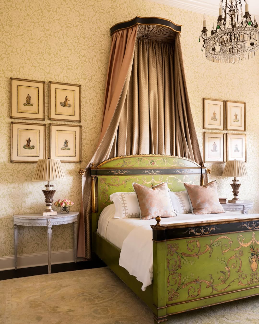 Elegant Victorian bedroom with a green, ornately painted bed, gold canopy, crystal chandelier, wallpaper, framed art, and matching side tables with lamps.