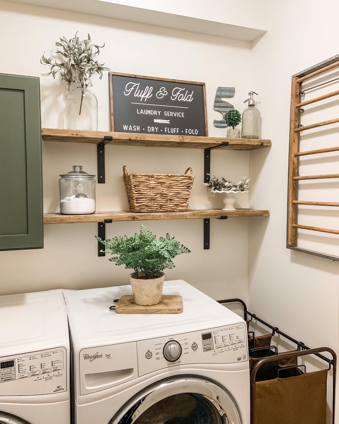 A laundry room with a washer and dryer, laundry room shelves displaying plants, jars, and baskets, and a sign that reads 