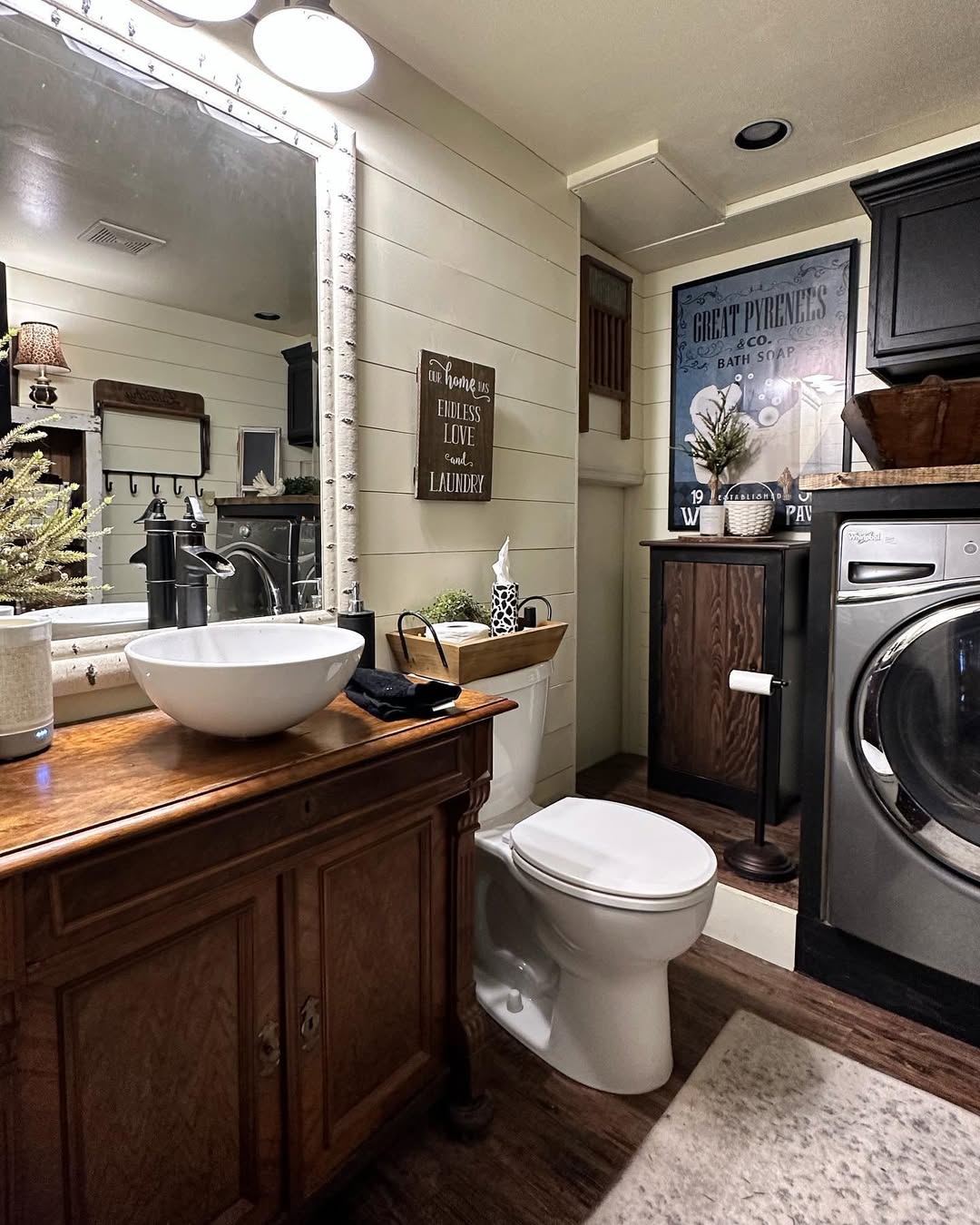 A bathroom with a wooden vanity, vessel sink, toilet, washer and dryer, framed wall art, and decorative plants—a perfect example of clever small bathroom design.