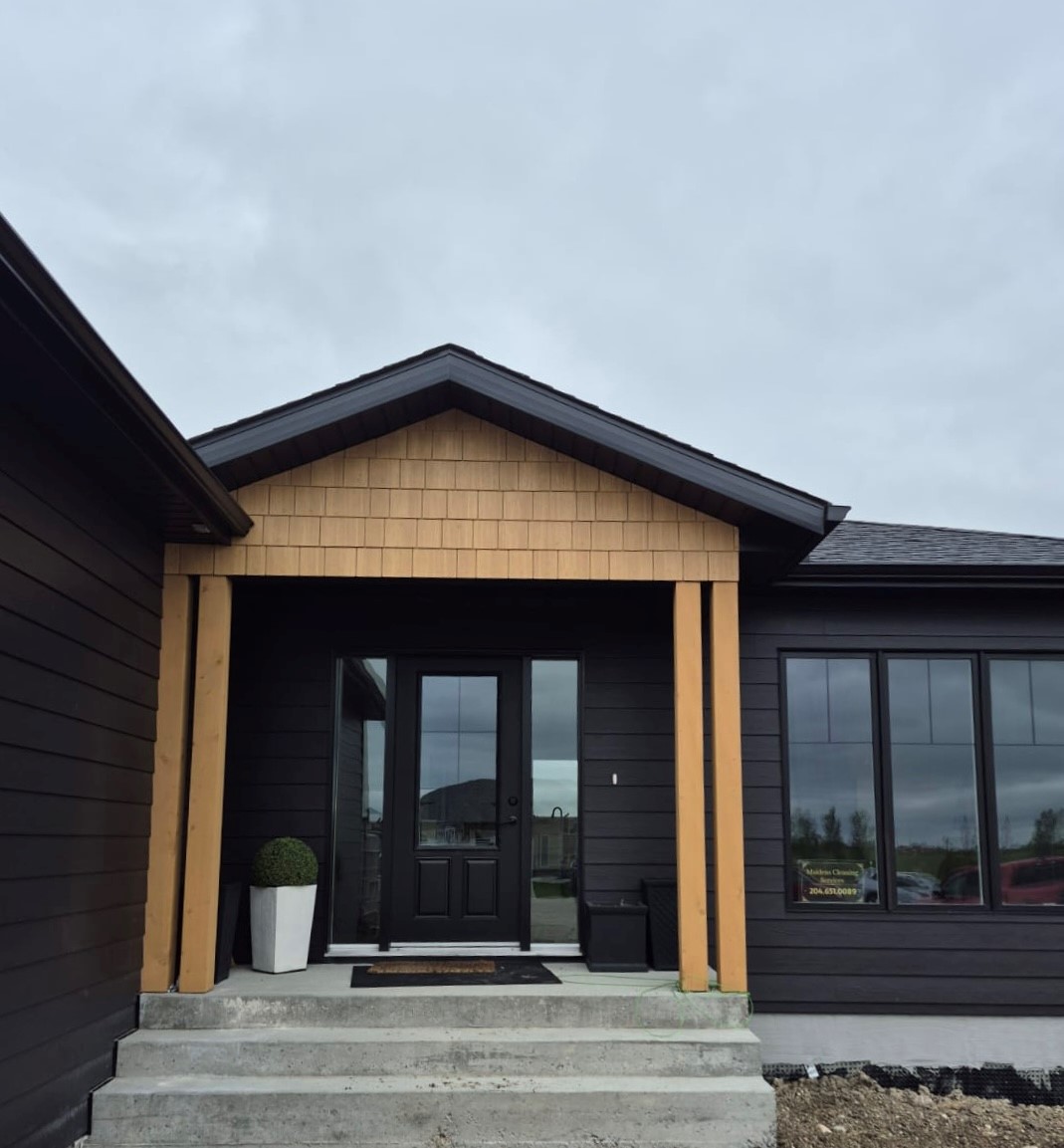 A modern farmhouse with a dark grey, almost Black house exterior features wooden beams, cedar house exterior accents, wooden shutters, stone columns, and festive holiday wreaths on the doors and windows.