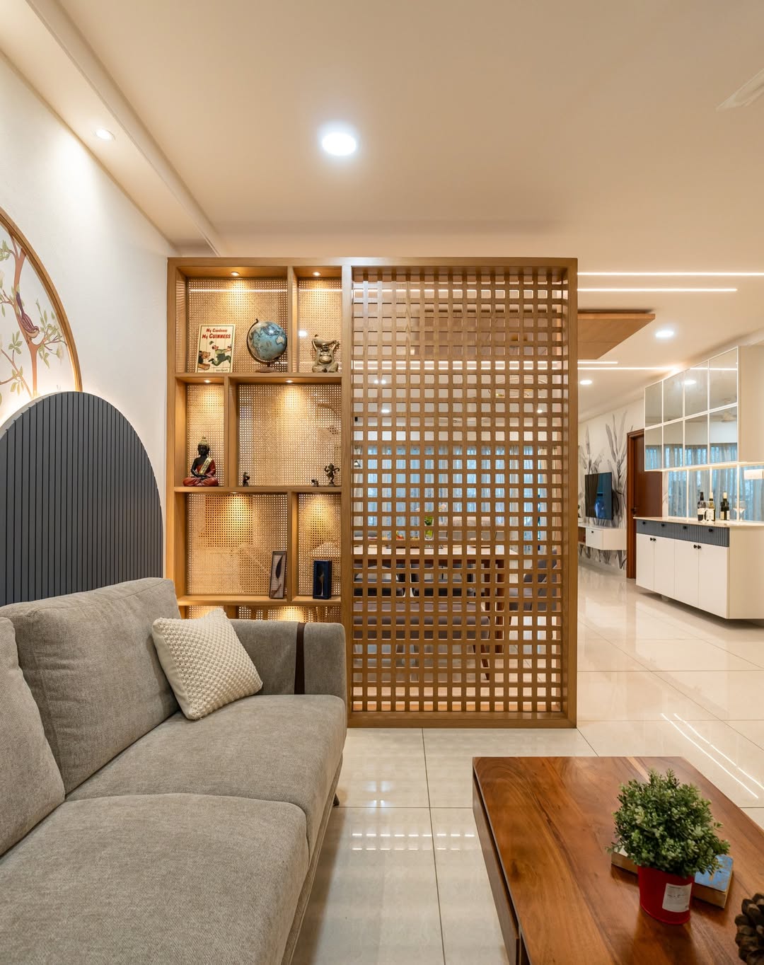 Modern living room with a gray sofa, wooden coffee table, and decorative shelving. A wooden lattice divider screen adds instant style while separating the space from the dining area and kitchen—perfect for stylish homeowners.