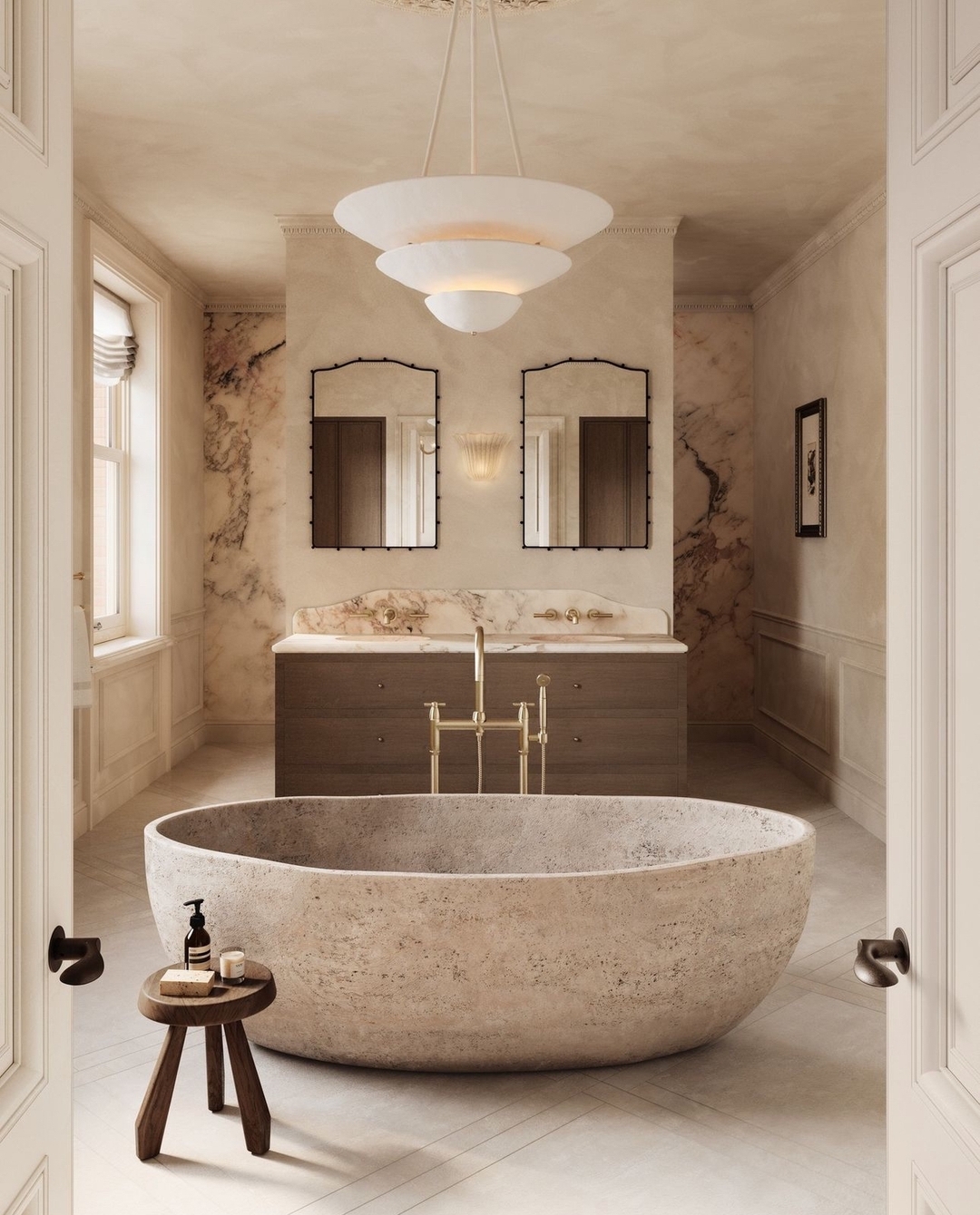 A freestanding stone bathtub is centered in a modern marble bathroom with double sinks, marble walls, mirrored cabinets, and a pendant light overhead. A small stool holds soap and a pump bottle, completing this elegant bathroom design.