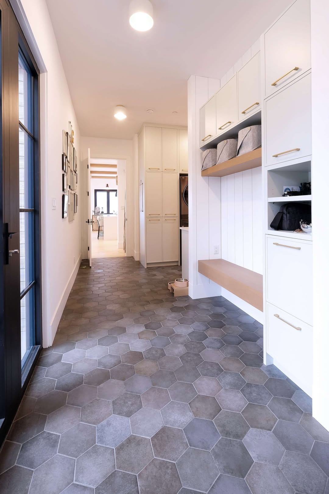 Modern hallway entryway with hexagonal tile flooring, built-in white cabinets, open shelving, and natural light from windows at the far end—perfect inspiration for genius mudroom ideas.