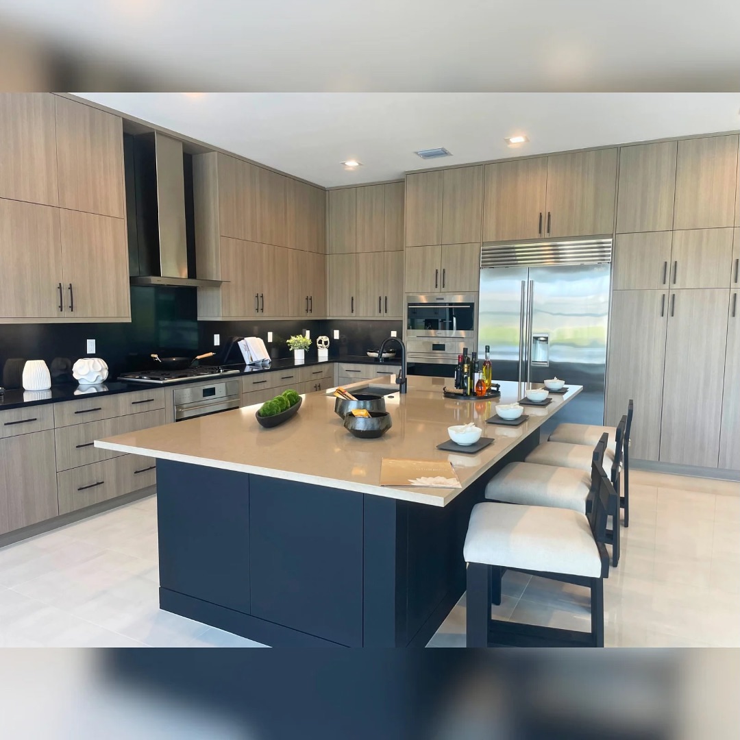 Modern kitchen with wood cabinetry, stainless steel appliances, a large island with stools, and neatly arranged dishes and utensils on the countertop.