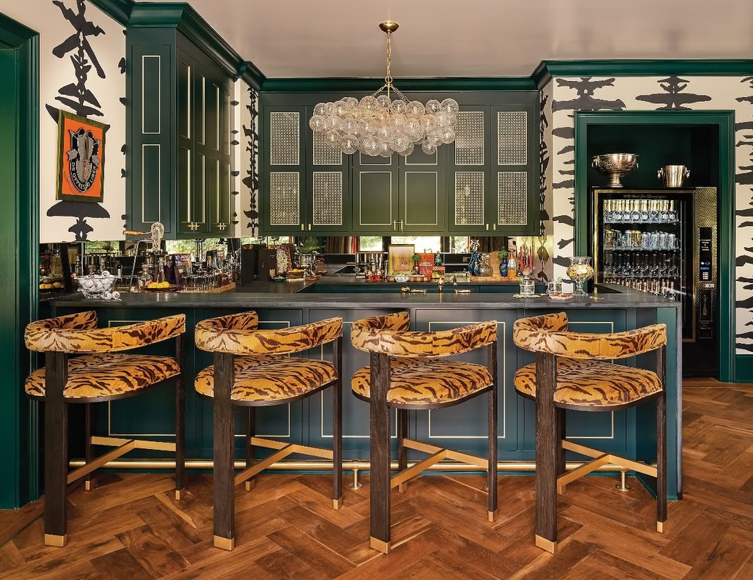 A stylish home bar with green cabinetry, a bubble chandelier, tiger-print barstools, and bold black-and-white abstract wallpaper inspires chic home bar ideas and unique bar decor.