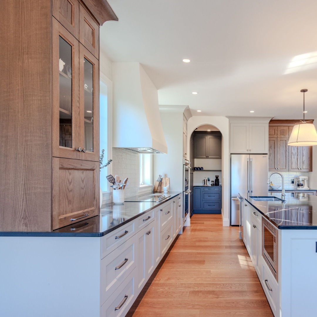 Modern kitchen with wood and white cabinetry, black countertops, stainless steel appliances, and light wood flooring under recessed lighting.