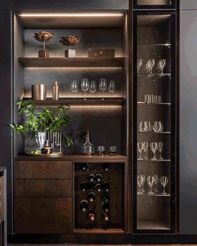 Modern home bar with glassware, wine bottles, metallic accessories, and decorative items neatly arranged on dark wood shelves and in a glass cabinet—perfect inspiration for gorgeous home bar ideas.