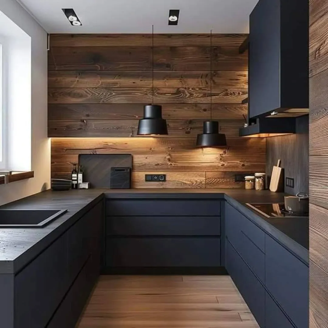 Modern kitchen with matte black cabinets, wooden walls, under-cabinet lighting, black pendant lights, and a built-in cooktop and sink. Natural light comes in from the left window.