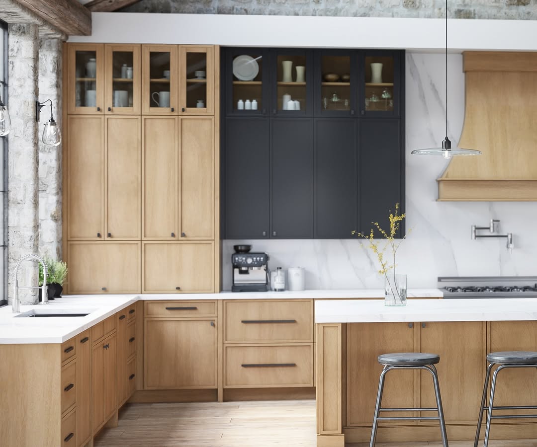 Modern kitchen with light wood cabinets, black upper cabinets, white countertops, pendant lights, a coffee maker, and two metal stools at an island.