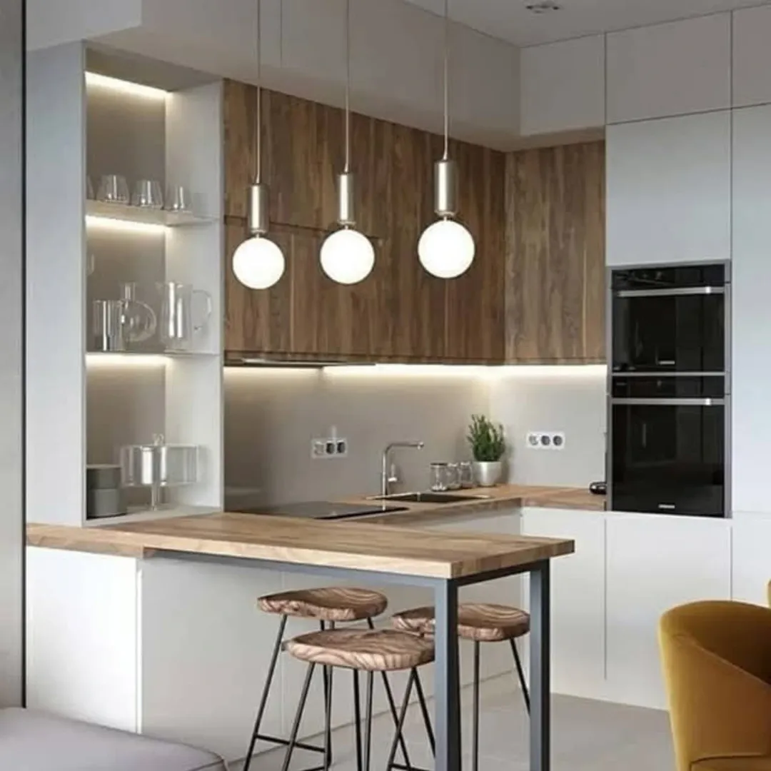 Modern kitchen with wood and white cabinetry, three round pendant lights, open shelves with glassware, built-in oven, and two stools at a wooden breakfast bar.