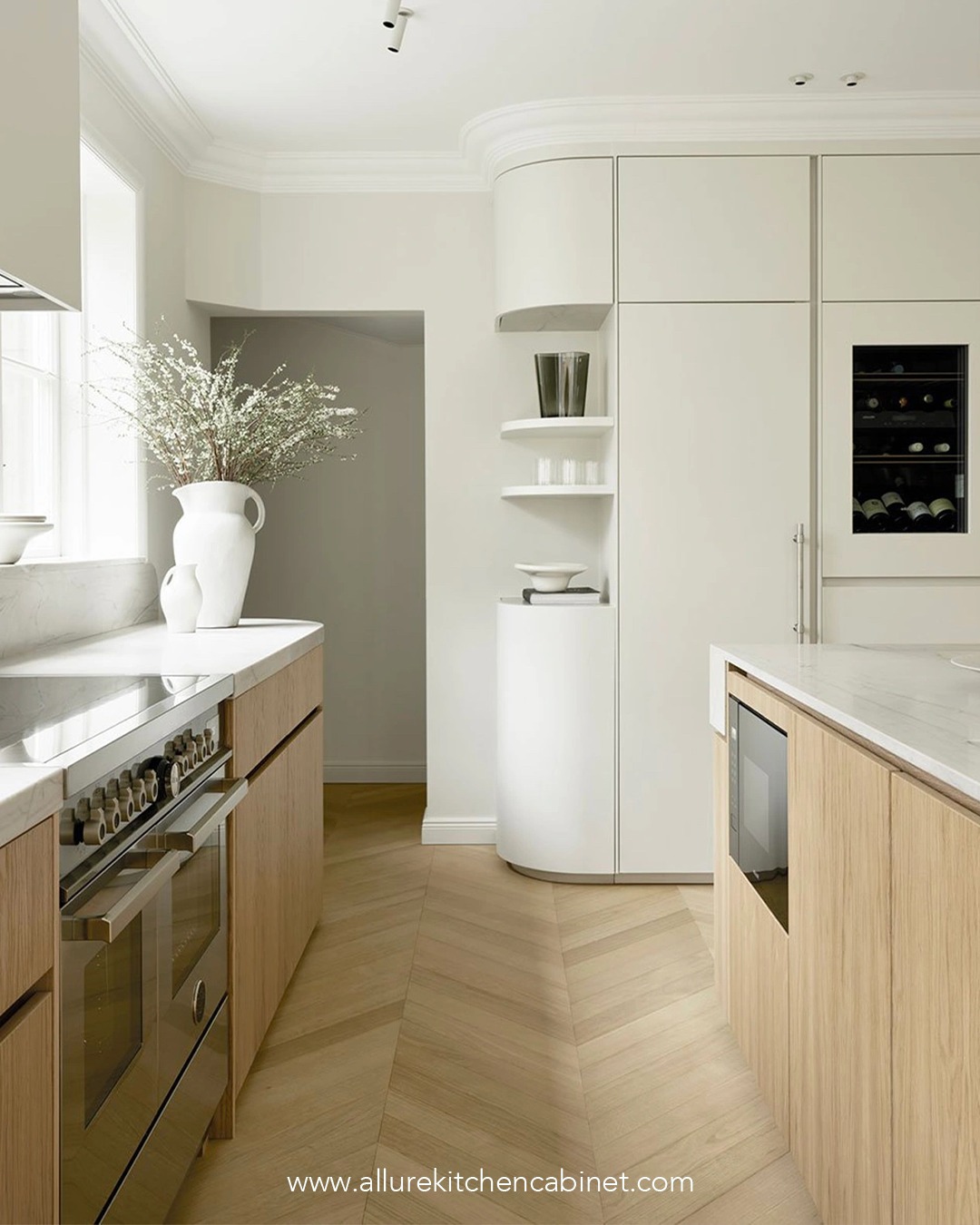 Modern kitchen with light wood cabinets, white countertops, built-in appliances, integrated fridge, open shelves, and a vase with flowers on a counter near a window.