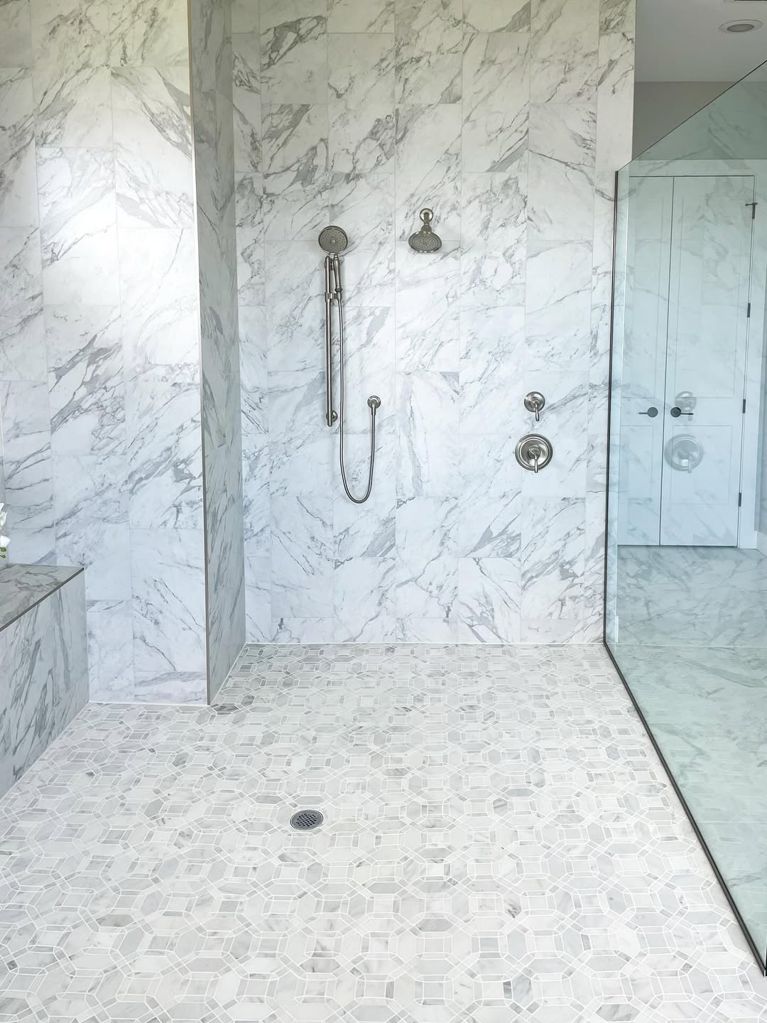 A modern walk-in shower with a striking marble design features tile walls and floor, a handheld showerhead, and a sleek glass enclosure—perfect for inspiring elegant bathroom ideas.
