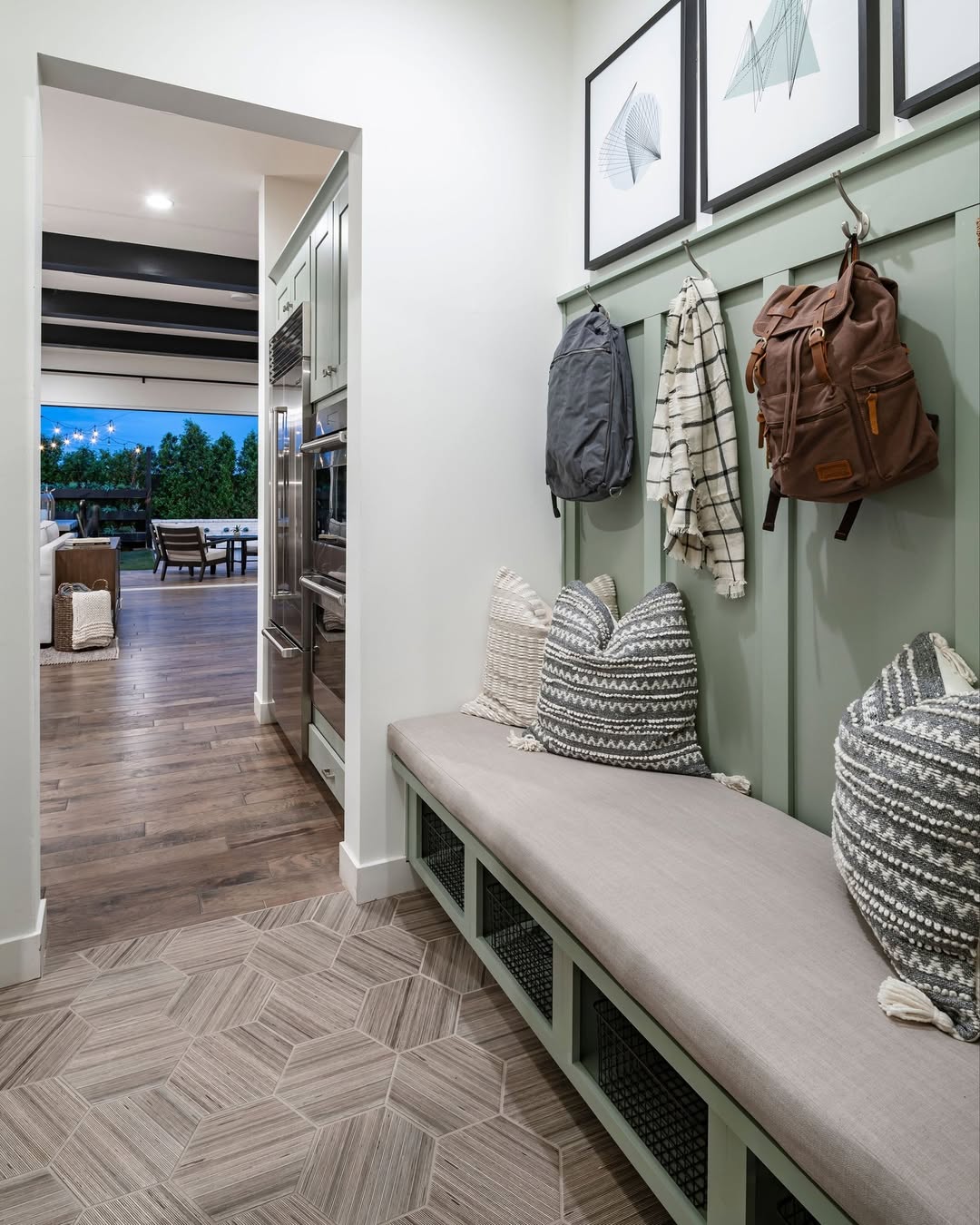 A stylish entryway with built-in bench seating, patterned pillows, hooks for bags and a shirt, and framed art on the wall offers smart mudroom ideas with an open view to the living and dining area.