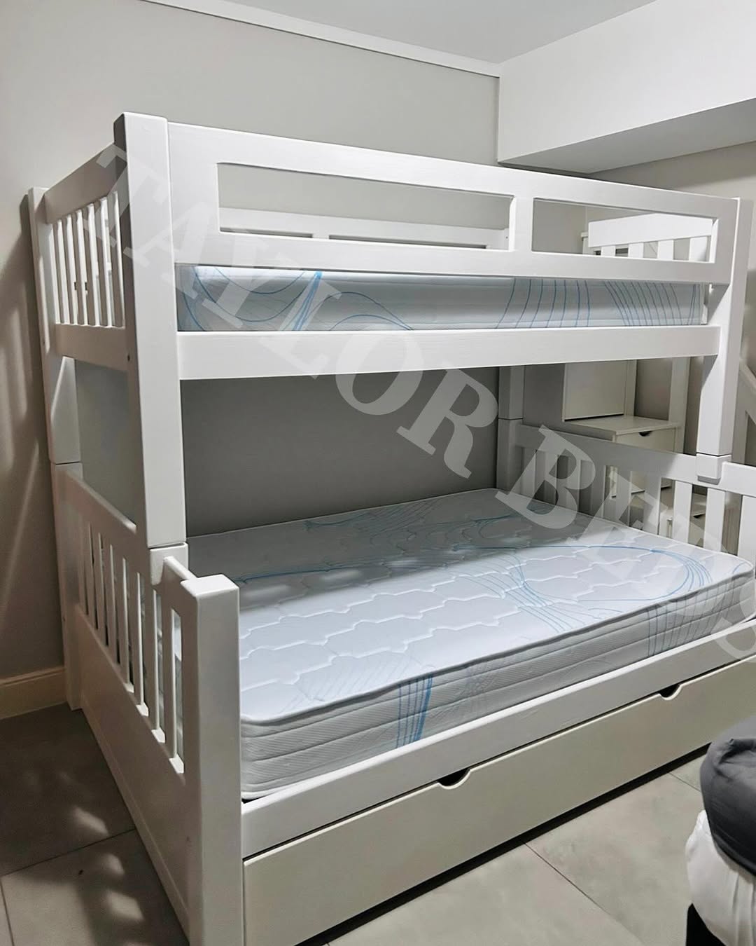 A white loft bed for small room features a twin mattress on top and a full mattress below, both without bedding, positioned against a light-colored wall.