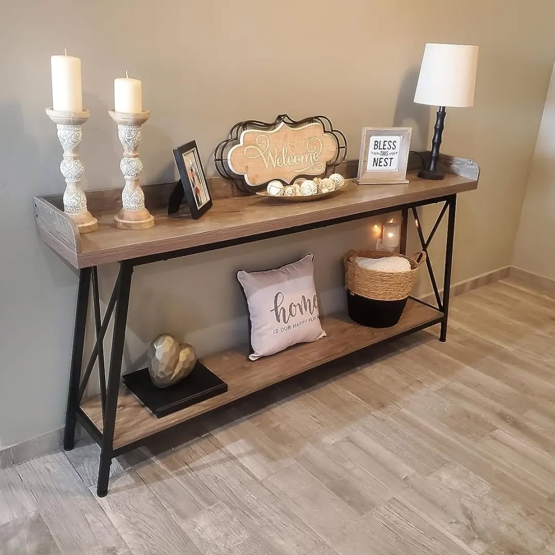 A wooden console table with entry table decor—lamp, candles, framed signs, a basket with a candle, decor pillow, and accents—set against a light wall on a wood floor.