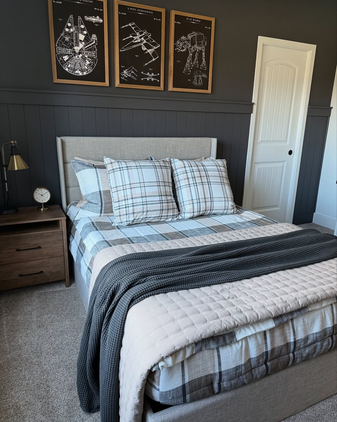 A neatly made bed with plaid bedding and a gray knit blanket in a modern teen boy bedroom; three framed Star Wars blueprints hang on the dark wall above the bed.