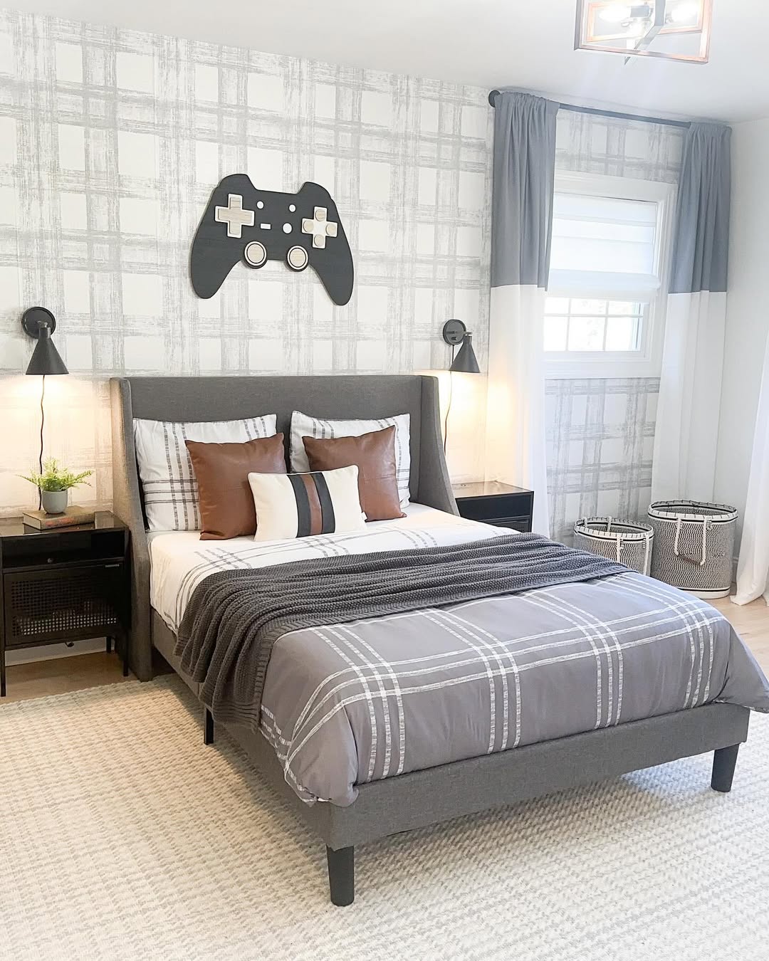 A modern teen boy bedroom with a gray plaid theme, a bed with striped pillows, black nightstands, and a large game controller wall decor above the headboard.
