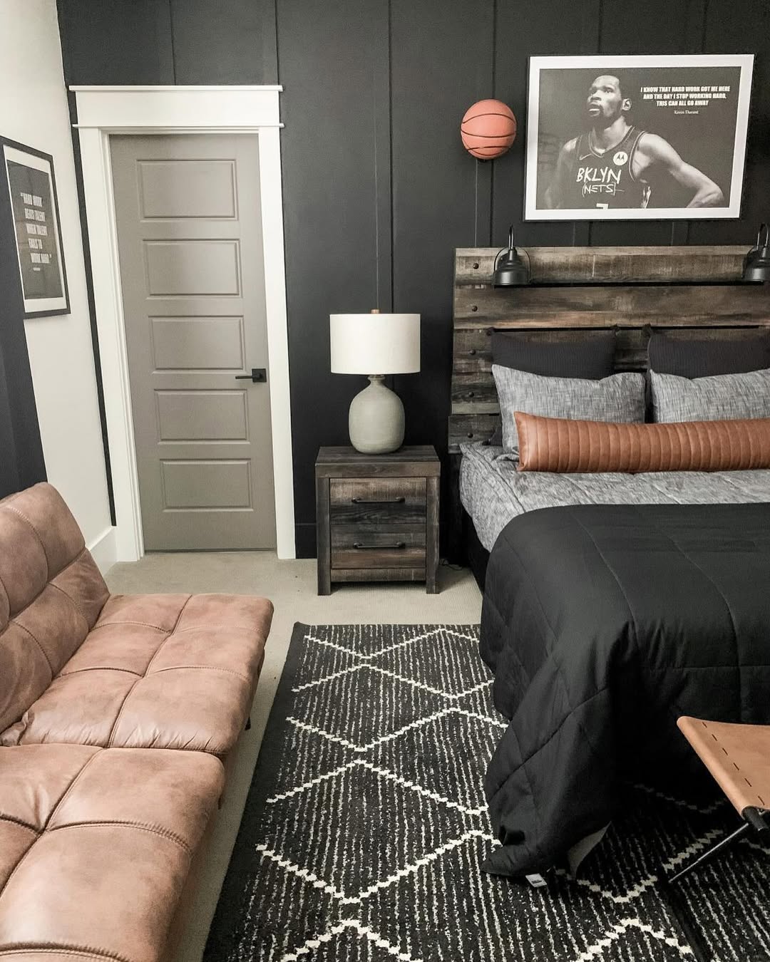 A modern teen boy bedroom with a black accent wall, wooden furniture, a brown futon, a geometric rug, and a framed basketball photo above the bed.