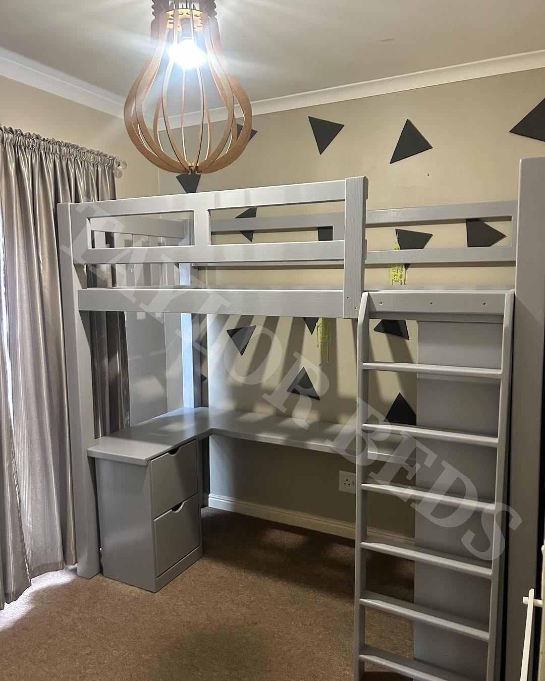 Gray loft bed for small room with built-in desk and storage beneath, positioned against a wall with black triangle decals; ladder on the side, curtain to the left, and modern light fixture overhead.