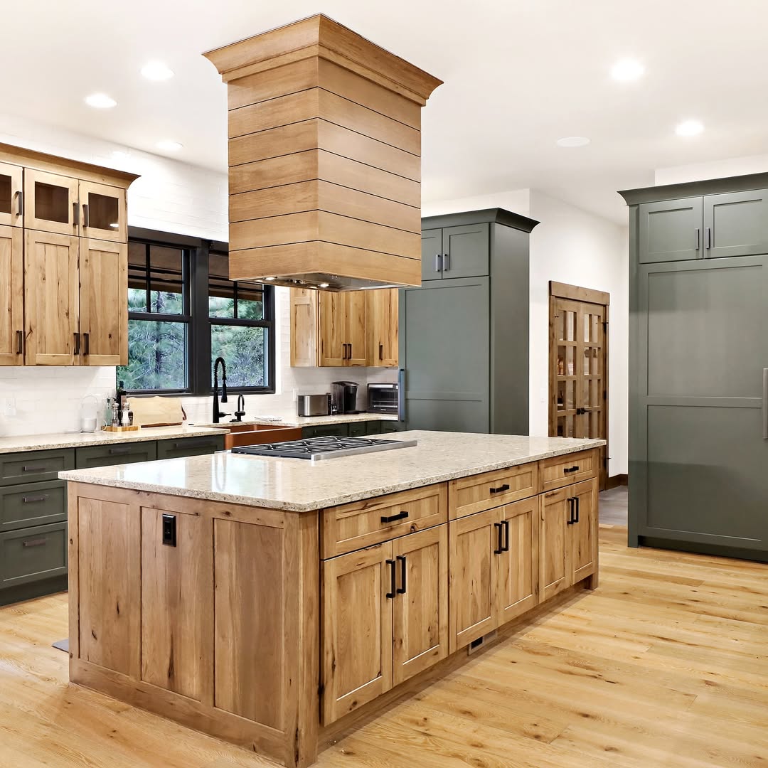 Modern kitchen featuring a large wooden island with a marble countertop, green cabinetry, stainless steel appliances, and wood flooring.
