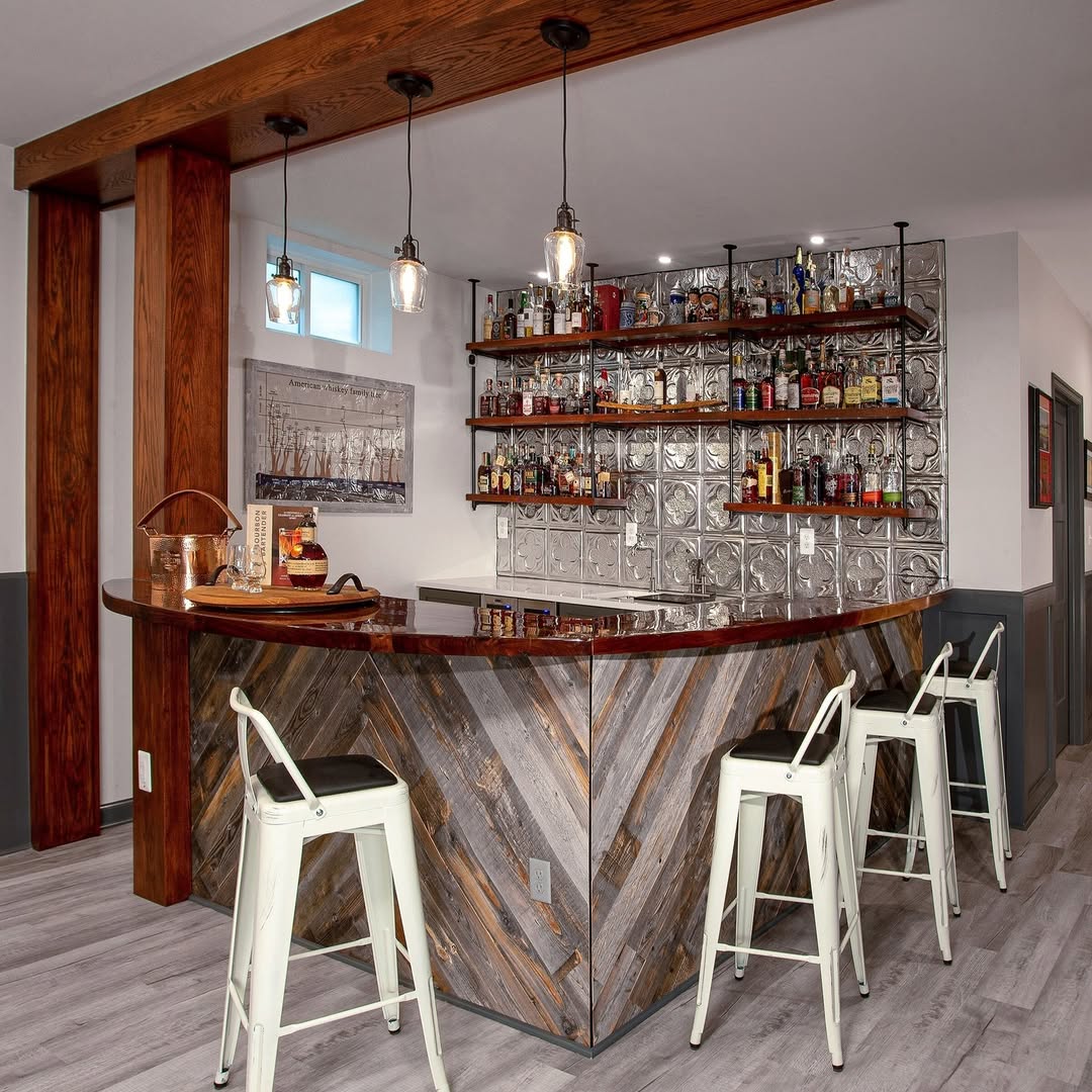 Home bar with a wood and glass block counter, three white metal stools, hanging pendant lights, and shelves stocked with various bottles and glasses—perfect inspiration for bar ideas for home.